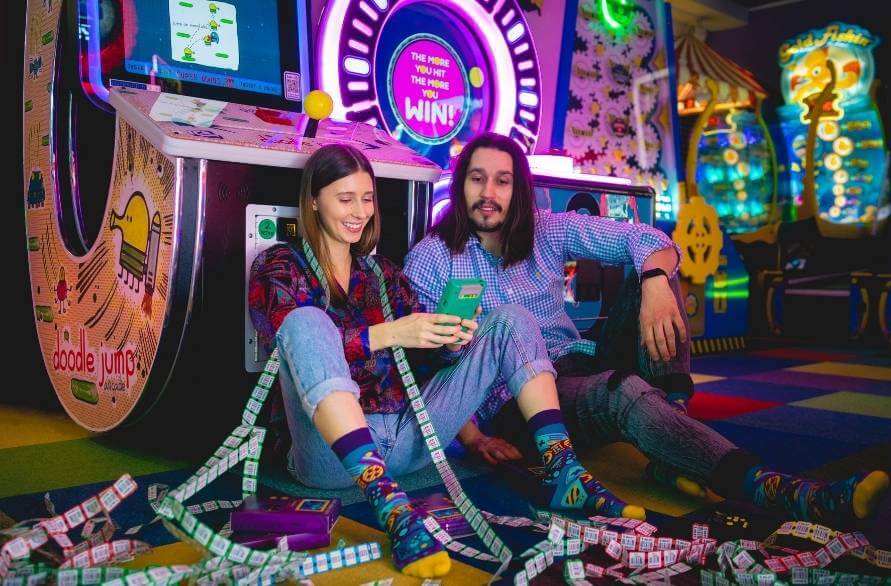 A man and woman in an amusement arcade with the Rainbow Game Socks on.